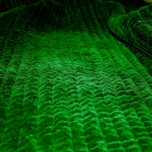 May include: Close-up of a deep green fabric with a textured, quilted pattern. The fabric has a soft, velvety texture.