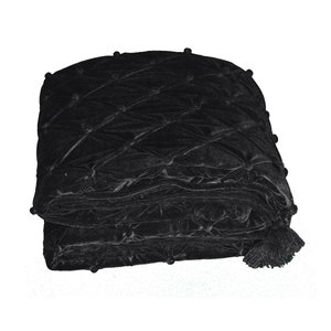 May include: A folded black velvet throw blanket with a diamond pattern and tufted accents. The blanket has a tassel on one corner and small, round embellishments at the intersections of the diamond pattern. The fabric has a soft, plush appearance.
