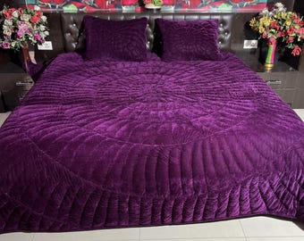 Puede incluir: Una colcha acolchada de terciopelo morado con un patrón circular. La colcha está sobre una cama con dos almohadas de terciopelo morado a juego.