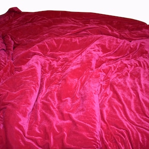 May include: A deep pink velvet blanket is draped over a bed, creating soft folds and wrinkles.