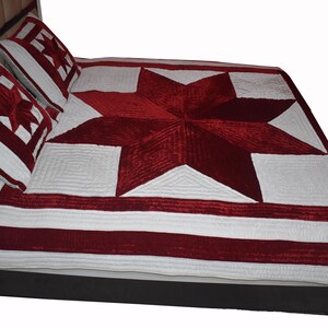 May include: A red and white quilted bedspread with a large star design. The bedspread is made of velvet and has a white border.