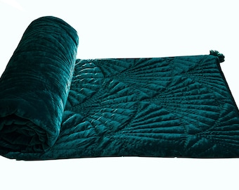 May include: A teal blue velvet quilted throw blanket with a geometric pattern. The blanket is rolled up on one end.