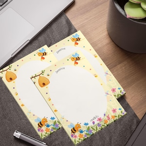 May include: Three personalized notepads with a bee theme. Each notepad features a yellow border with bees, flowers, and stars. The name "Jessica" is printed at the top. A pen and laptop are in the background.