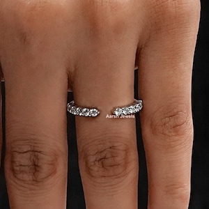 May include: A silver ring with a row of small clear stones set in a curved band.