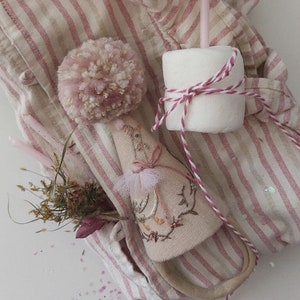 K&ouml;nnte beinhalten: Ein rosa-wei&szlig; gestreiftes Stoff mit einem rosa Bommel, einem kleinen gestickten Vogel und einem wei&szlig;en Marshmallow mit rosa-wei&szlig;em Garn. Es gibt auch rosa-wei&szlig;e Kerzen und rosa Glitzer auf dem Stoff.