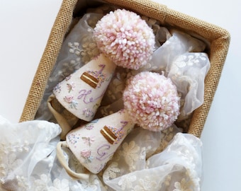 May include: Two white party hats with pink pom poms on top. The hats are decorated with embroidered flowers and the text "Happy Birthday".