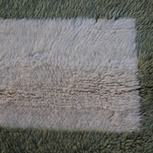 May include: A close-up of a fluffy rug with a square patch of a different color. The rug is green and the patch is white.
