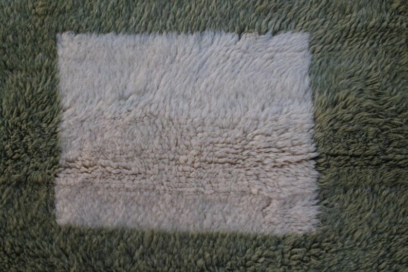 May include: A close-up of a fluffy rug with a square patch of a different color. The rug is green and the patch is white.
