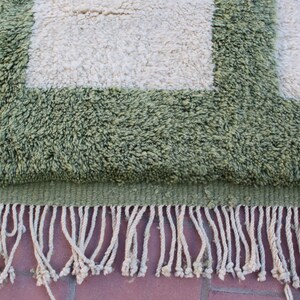 May include: A green and white rug with a fringe border. The rug has a geometric pattern with squares.