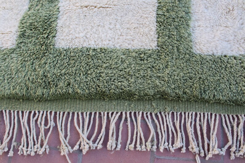 May include: A green and white rug with a fringe border. The rug has a geometric pattern with squares.