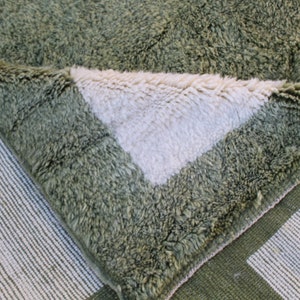 May include: Close-up of a green and white woven rug with a fuzzy texture. The rug is folded over, revealing the white underside.