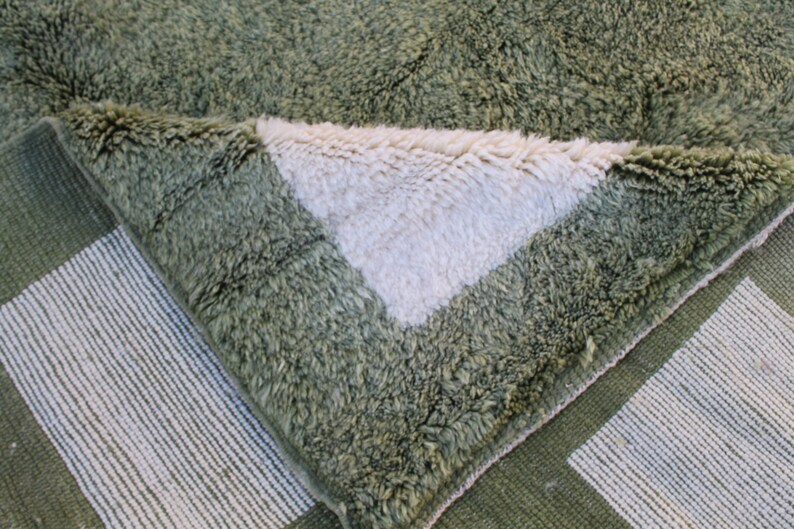 May include: Close-up of a green and white woven rug with a fuzzy texture. The rug is folded over, revealing the white underside.