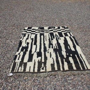 May include: Black and white abstract rug with a geometric pattern. The rug has a fringe border.