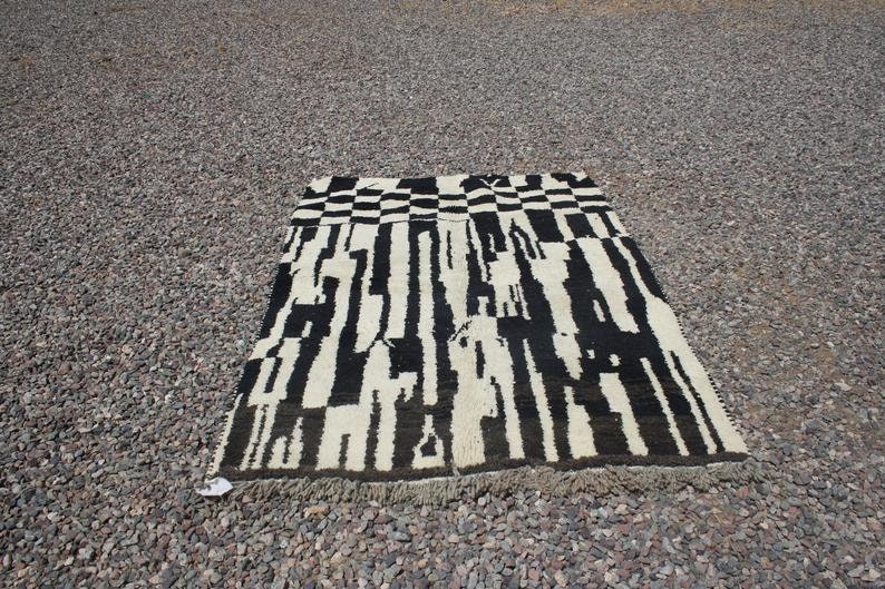 May include: Black and white abstract rug with a geometric pattern. The rug has a fringe border.