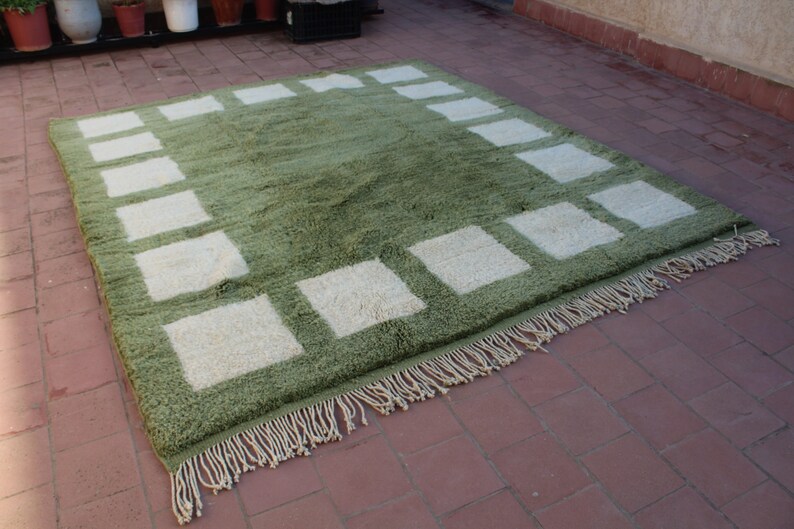 May include: A green and white area rug with a geometric pattern. The rug has a fringe border.