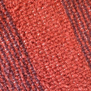 May include: Close-up of a woven fabric with a red and dark brown striped pattern. The fabric has a textured, fuzzy surface.