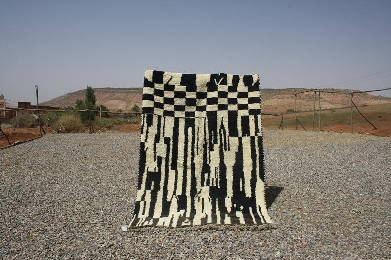 May include: Black and white rug with a geometric pattern. The rug is made of wool and has a hand-woven texture.