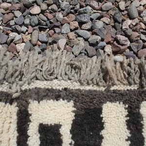 May include: Close-up of a white and black striped rug with a fringe border. The rug is made of wool and has a textured surface.