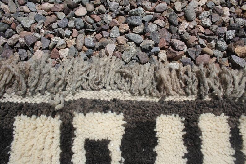 May include: Close-up of a white and black striped rug with a fringe border. The rug is made of wool and has a textured surface.