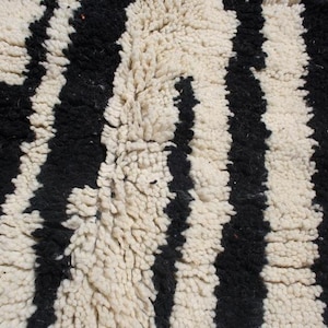 May include: Close-up of a black and white striped rug with a fluffy texture. The rug is made of wool and has a traditional Moroccan design.