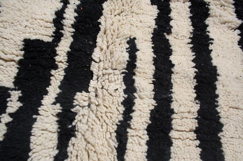 May include: Close-up of a black and white striped rug with a fluffy texture. The rug is made of wool and has a traditional Moroccan design.