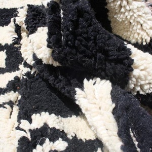 May include: Close-up of a black and white woven rug with a shaggy texture. The rug has a geometric pattern and is made of wool.