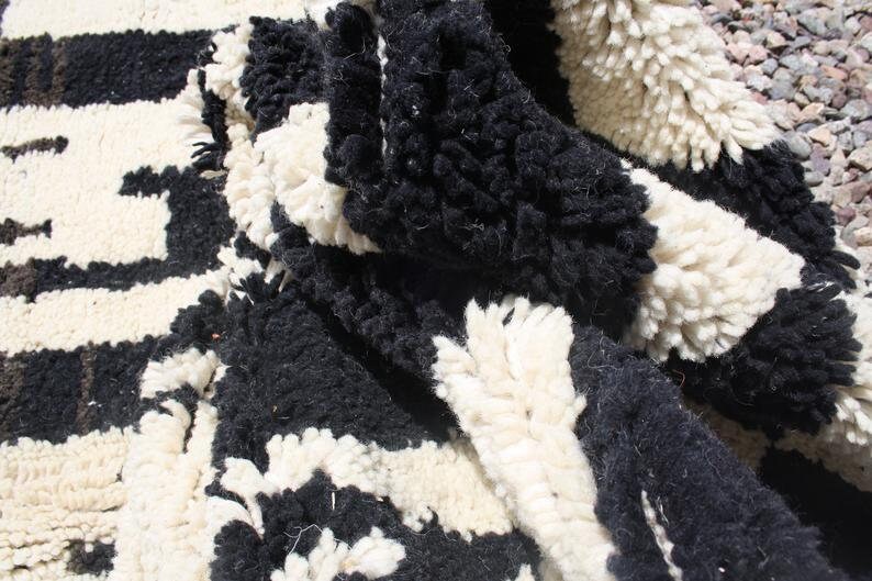 May include: Close-up of a black and white woven rug with a shaggy texture. The rug has a geometric pattern and is made of wool.