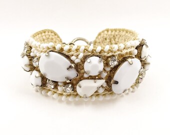 May include: A white crocheted bracelet with white and clear rhinestones. The bracelet is decorated with large white stones.