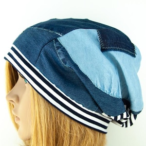 May include: A blue denim beanie with a white and black striped band. The beanie is made of different pieces of denim sewn together.
