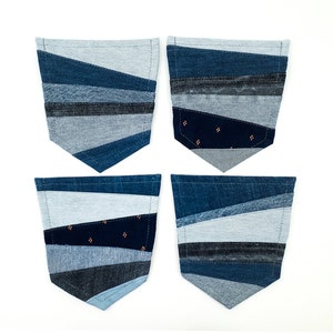 Op de afbeelding: Vier denim zakken met een patchwork ontwerp. Elke zak heeft een unieke opstelling van blauwe denim stukken, waardoor een geometrisch patroon ontstaat. De zakken zijn in tinten licht- en donkerblauw, sommige met een patroonstof.