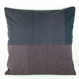 May include: A square decorative pillow with a patchwork design. The top half is a solid dark gray fabric, while the bottom half features a patterned, dark burgundy and gray fabric. A section of dark blue fabric is on the right side.