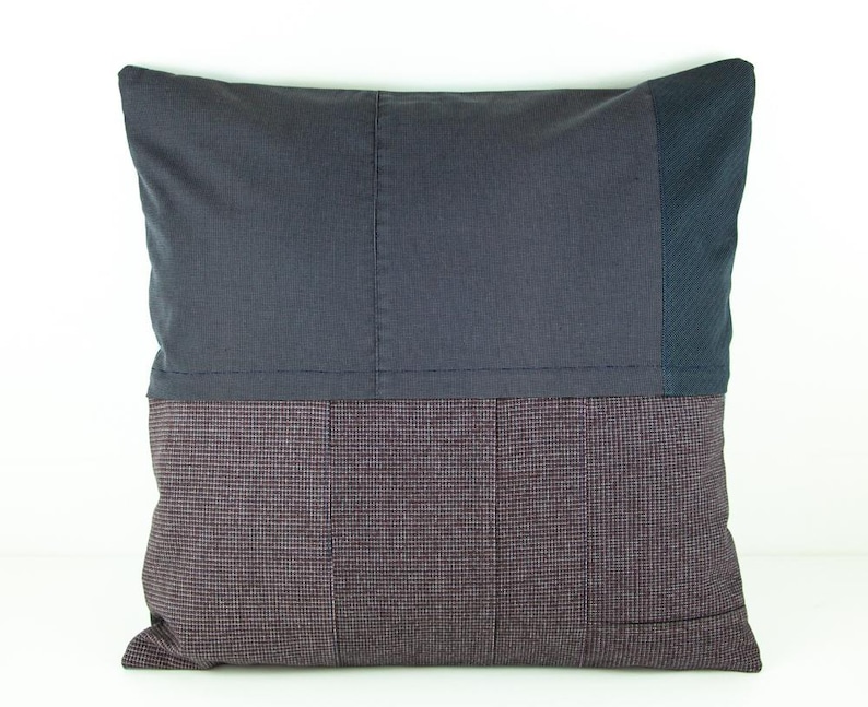 May include: A square decorative pillow with a patchwork design. The top half is a solid dark gray fabric, while the bottom half features a patterned, dark burgundy and gray fabric. A section of dark blue fabric is on the right side.