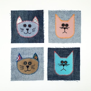 May include: Four square denim fabric patches featuring appliqued cat faces. The cats are crafted from various coloured fabrics including blue and white stripes, solid pink, brown, and bright turquoise, with button eyes and stitched details.