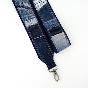 Peut inclure: Une sangle en patchwork de denim avec un dos bleu foncé et un fermoir en métal. La sangle est composée de différentes nuances de denim bleu, cousues ensemble dans un motif patchwork. Le fermoir en métal est de couleur bronze.