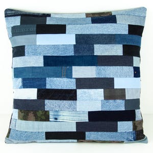 May include: Square decorative pillow with a patchwork design made from various shades of blue denim. The pillow features a rectangular pattern, with each rectangle a different shade of blue. The pillow is a square shape.