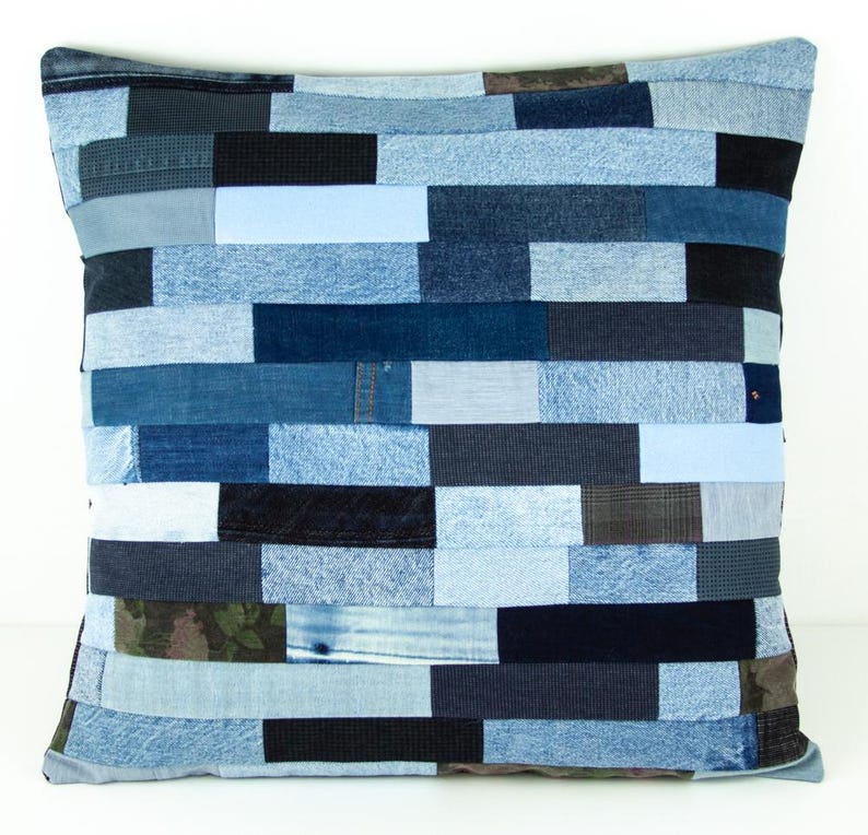 May include: Square decorative pillow with a patchwork design made from various shades of blue denim. The pillow features a rectangular pattern, with each rectangle a different shade of blue. The pillow is a square shape.