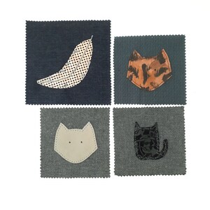 May include: Four fabric squares with appliqued designs. One square features a feather with a black and white polka dot pattern. The other three squares have cat face designs in tan, light gray, and black floral patterns. The squares are on a white background.