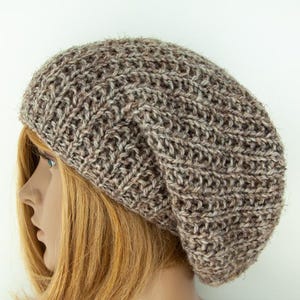 May include: A brown and beige knitted beanie hat. The hat is made of textured yarn and has a slouchy fit. The hat is shown on a mannequin with blonde hair. The hat is a neutral colour and can be worn with many outfits.