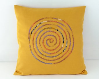 Può includere: Un cuscino giallo senape con un design a spirale cucito multicolore al centro.