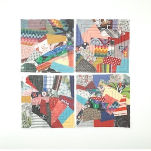 Op de afbeelding: Vier vierkante stoffen kunstwerken, elk met een uniek patchwork ontwerp. De patches hebben een verscheidenheid aan kleuren en patronen, waaronder bloemen, strepen en effen kleuren. Elke vierkant is omrand met een gestikte rand.