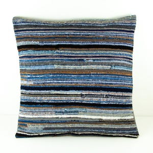 Pode incluir: Uma almofada decorativa com um padrão listrado feito de tecido de ganga reciclado. A almofada é azul, castanho e branca.