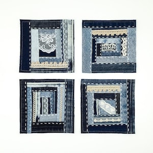 Pode incluir: Quatro porta-copos quadrados feitos de retalhos de tecido jeans em vários tons de azul. Cada porta-copos apresenta um padrão de colcha log cabin com costuras decorativas brancas, tiras integradas de renda creme e detalhes de renda floral.