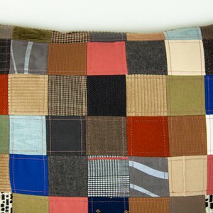 Puede incluir: Un coj&iacute;n patchwork con una variedad de cuadrados de tela en tonos de rojo, azul, verde, marr&oacute;n y gris. Los cuadrados est&aacute;n cosidos, creando una superficie texturizada. El dise&ntilde;o es una mezcla de patrones y texturas.