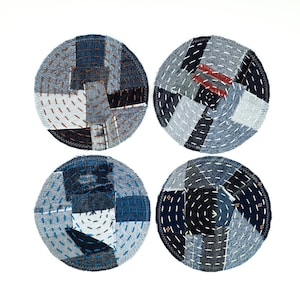 Può includere: Quattro sottobicchieri rotondi in denim con diversi disegni di patchwork e cuciture. Ogni sottobicchiere presenta una combinazione unica di ritagli di tessuto denim blu cuciti insieme in un motivo circolare.