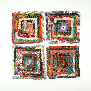 May include: Four handmade, square fabric coasters. Each coaster has a spiral design made from a variety of colourful fabric scraps, including red, orange, green, and blue. The coasters are arranged on a white background.