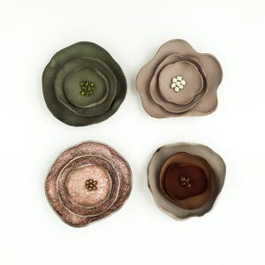 Peut inclure: Quatre broches faites à la main en forme de fleur, dans des tons de vert, taupe, cuivré et marron. Chaque broche présente des pétales superposés et un centre perlé, sur fond blanc. Ces accessoires uniques ajoutent une touche d'élégance inspirée de la nature.