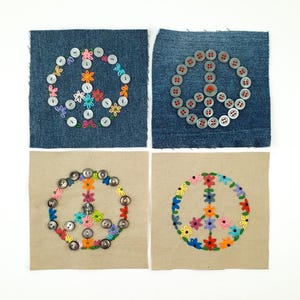 Può includere: Quattro quadrati di tessuto con simboli di pace. Due quadrati sono in denim e due sono beige. I simboli di pace sono creati con bottoni e fiori ricamati in vari colori. I bottoni sono argentati e i fiori sono rosa, arancioni, gialli e blu.