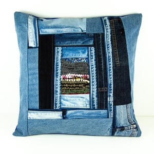 Puede incluir: Cojín cuadrado de mezclilla con diseño de patchwork. El cojín presenta varios tonos de mezclilla azul, con un panel central rectangular de telas mixtas. Los detalles en mezclilla azul oscuro y negro crean un aspecto texturizado y artesanal. Medidas en centímetros.