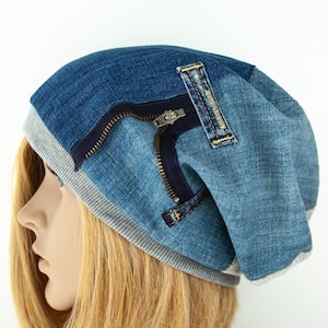 May include: A blue denim beanie hat with a grey brim and a zip detail. The hat is made of different shades of blue denim and has a patch detail near the zip. The hat is shown on a mannequin head.