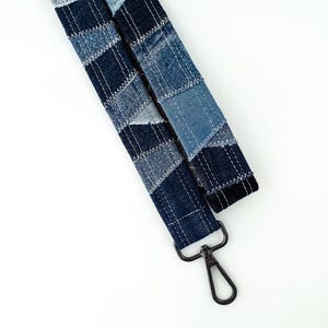 May include: A denim lanyard with a patchwork design in various shades of blue. The lanyard features a metal clasp for attaching keys or an ID badge. The fabric is stitched together with white thread, creating a textured appearance.